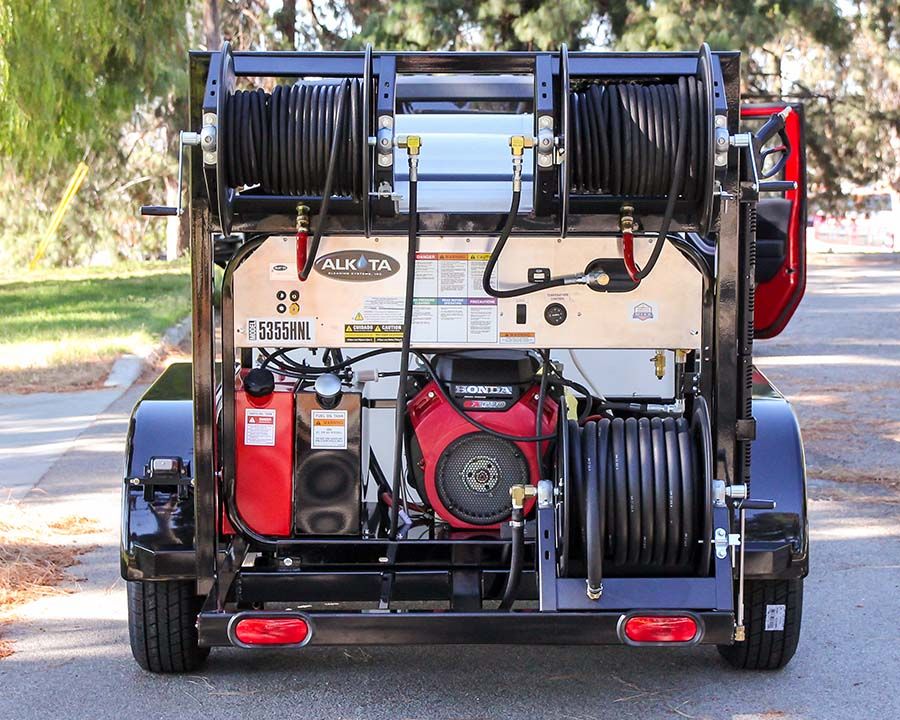 The rear of a trailer with an Alkota 5355HNL hot water machine, a Honda engine and three hose reels