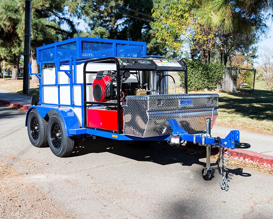 An Alkota hot water machine on a blue tandem with a caged tank and a diamond-plate toolbox