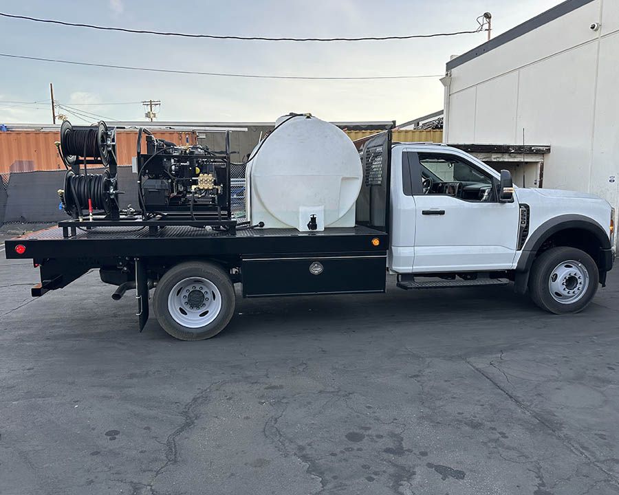 White flatbed truck carrying a hot-water skid, two hose reels and a large round tank