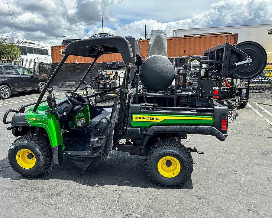 Hot-water skid with a burner, tank and hose reel built into the bed of a green utility vehicle