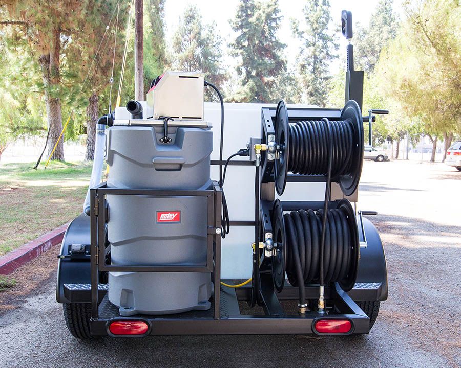 The rear of a black trailer with a gray Hotsy tank in a frame and two hose reels