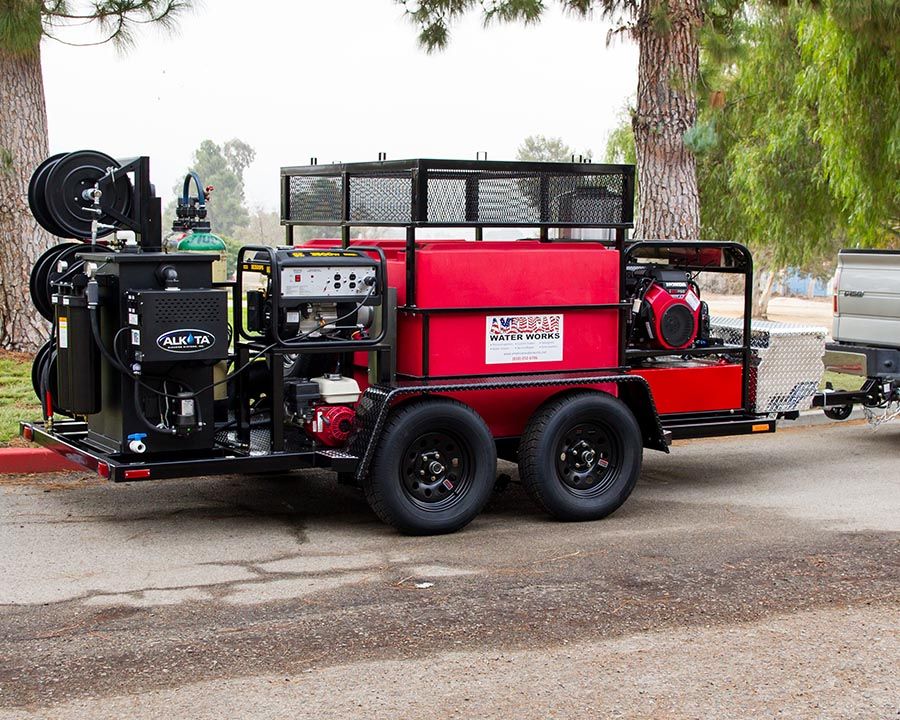 A black tandem with a red tank under a cage, an Alkota unit and reels at the back, and a Honda-powered machine up front