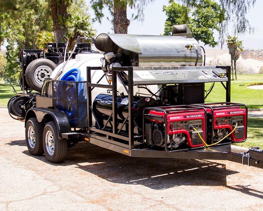 An Alkota hot water machine and two Honda generators on a black tandem trailer, with a spare tire and reels at the back