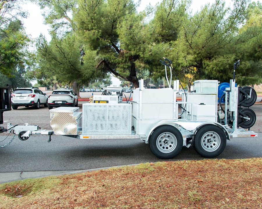 White tandem-axle trailer with a long tank, a diamond-plate toolbox, a mesh cage and side-mounted hose reels